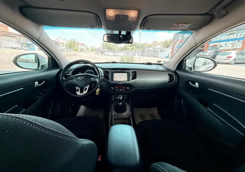 Vue intérieure avant du Kia Sportage 2015, tableau de bord noir avec volant multifonction et boîte manuelle.