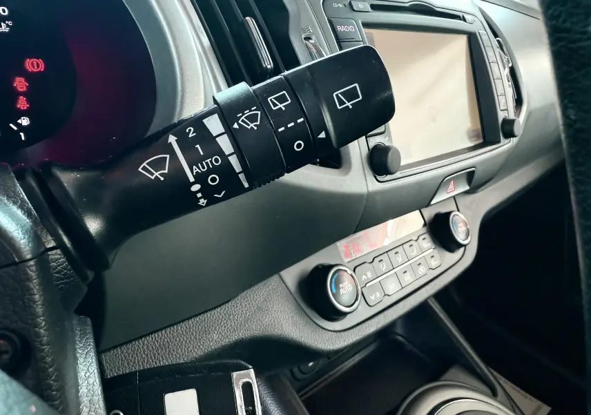 Gros plan sur la commande d’essuie-glace et le tableau de bord gris noir du Kia Sportage 2015 diesel blanc.