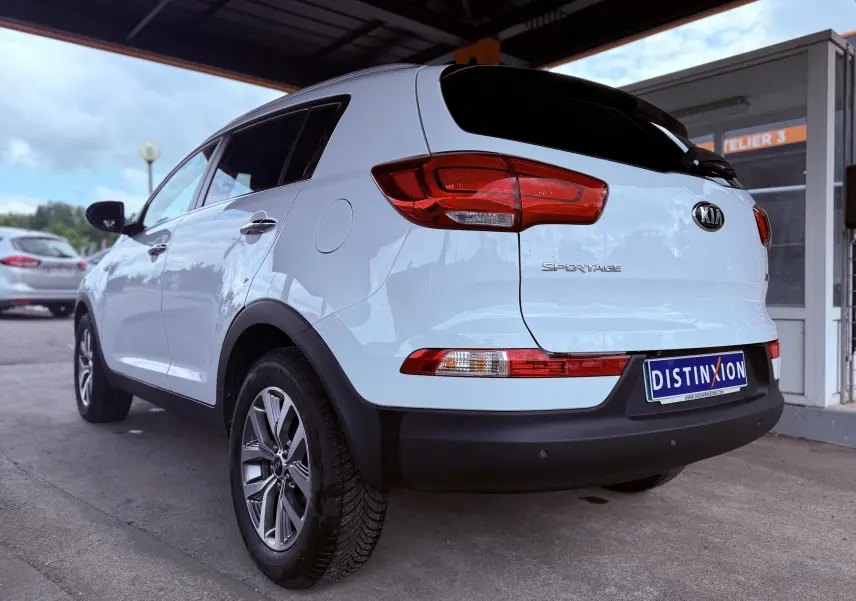Vue 3/4 arrière droite d'un Kia Sportage blanc avec feux arrière rouges et jantes alliage grises.
