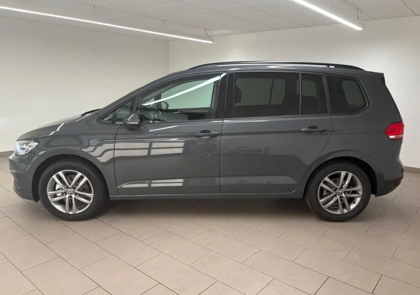 Profil côté gauche d'un Volkswagen Touran gris dauphin 2025, version 7 places avec jantes alliage 17 pouces en intérieur lumineux.