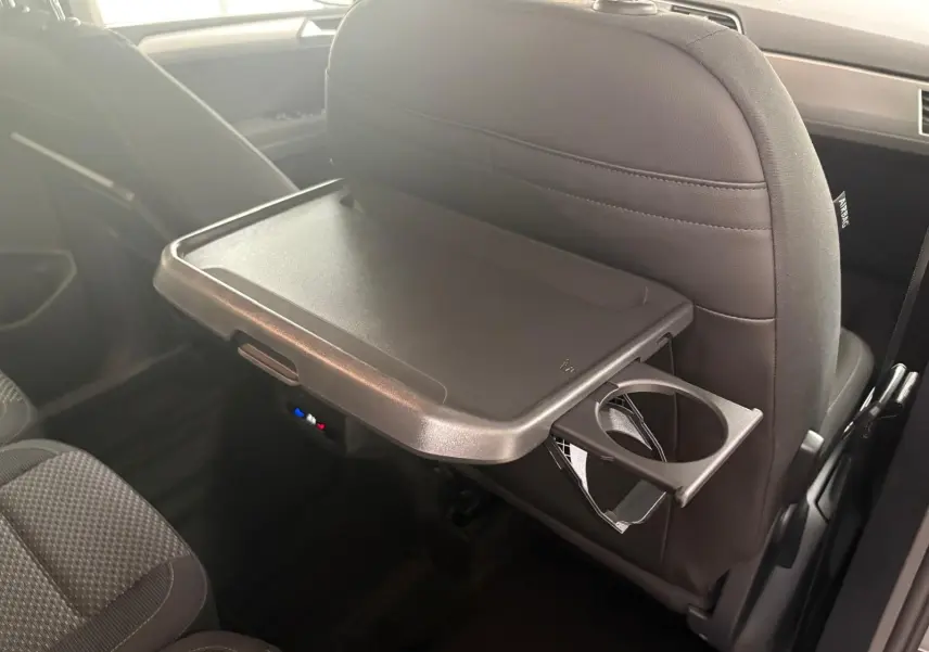 Tablette rabattable avec porte-gobelet fixée au dossier avant dans l'habitacle du Volkswagen Touran gris dauphin 2025.