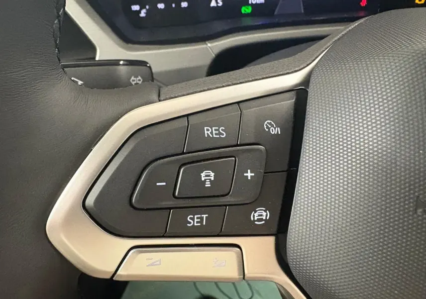 Gros plan sur les commandes au volant gauche du Volkswagen Touran gris dauphin, avec régulateur de vitesse adaptatif.