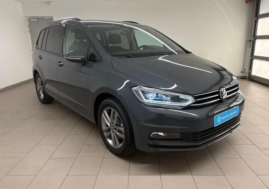 Volkswagen Touran gris dauphin en 3/4 avant droit, avec phares LED allumés et jantes alliage 17 pouces.