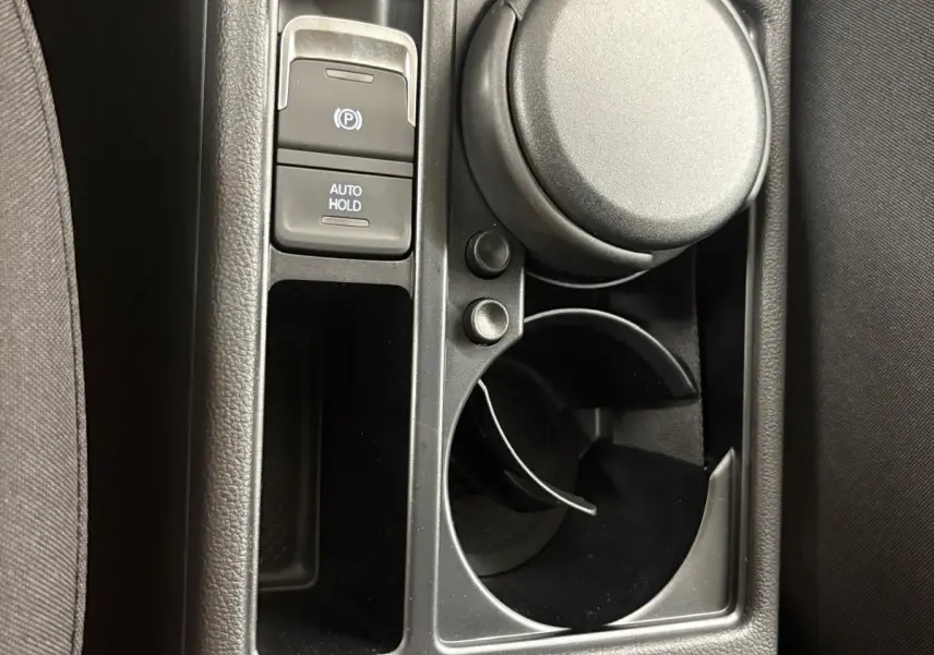 Gros plan sur la console centrale noire du Volkswagen Touran 2025, avec frein à main électrique et porte-gobelet.