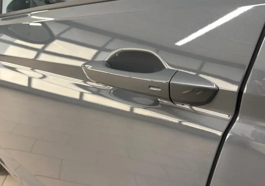 Poignée de porte côté gauche gris dauphin du Volkswagen Touran 2025, finition VW Edition, reflet intérieur lumineux.