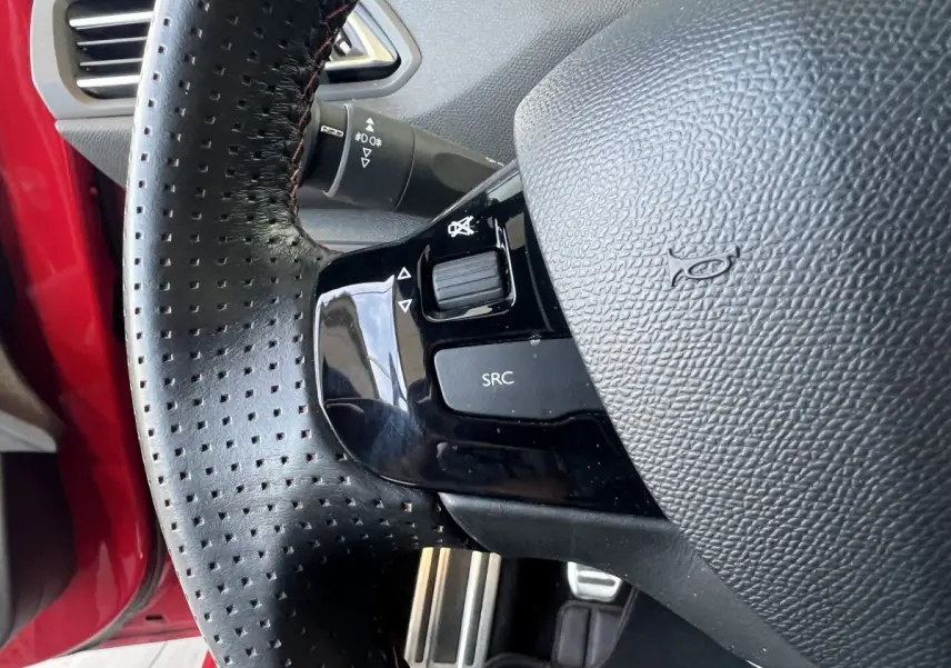 Gros plan sur le volant cuir perforé de la Peugeot 308 GT Line rouge, avec commandes audio intégrées.