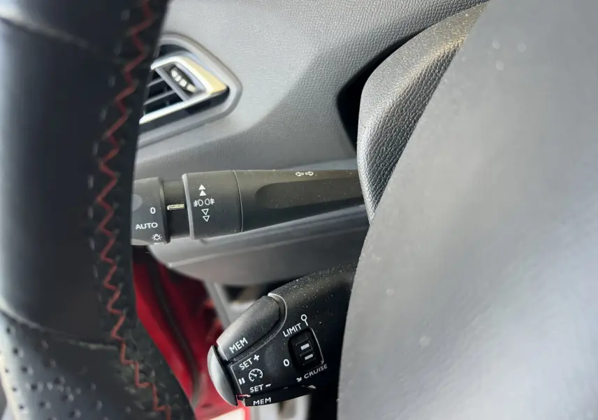 Gros plan sur commandes au volant cuir noir avec surpiqûres rouges dans Peugeot 308 GT Line rouge, côté gauche.