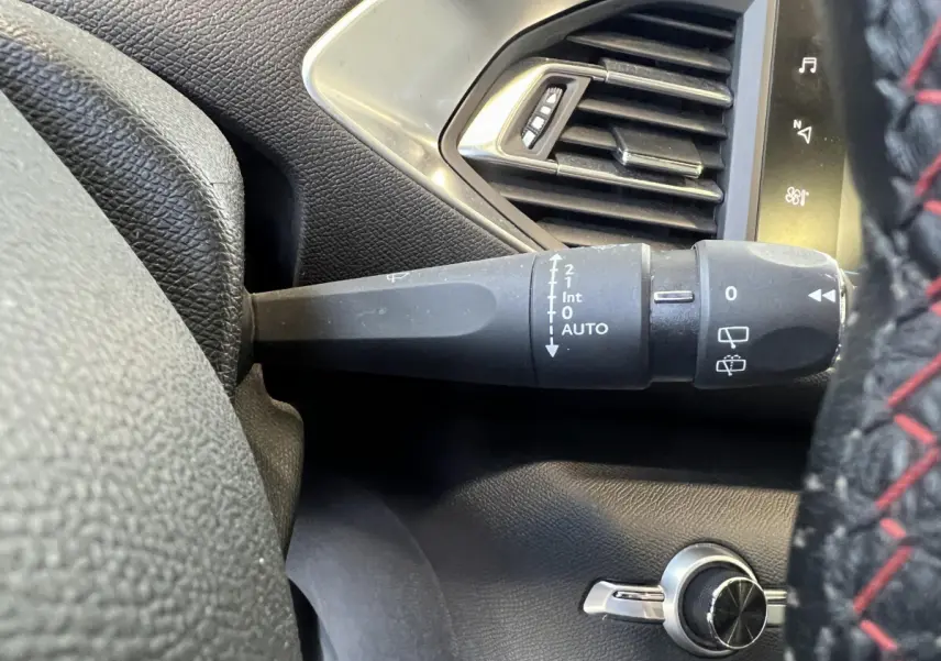 Gros plan sur la commande d’essuie-glace à gauche du volant cuir avec surpiqûres rouges dans un Peugeot 308 rouge.