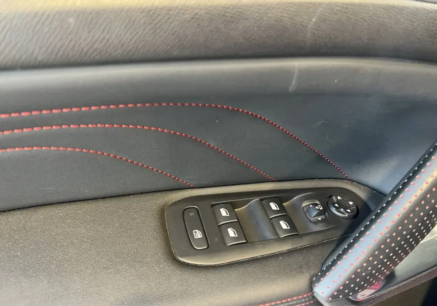 Gros plan sur la commande des vitres électriques côté conducteur avec surpiqûres rouges dans une Peugeot 308 GT Line rouge.