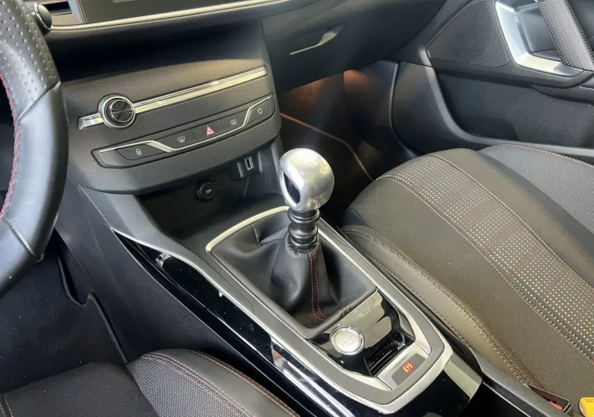 Vue rapprochée de la console centrale d'une Peugeot 308 GT Line rouge avec levier de vitesse manuel et bouton démarrage.