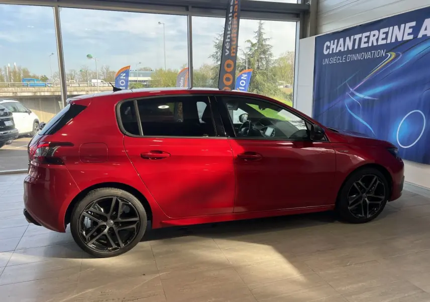 Profil latéral droit d'une Peugeot 308 Puretech 130 S&S GT Line rouge brillante avec jantes alliage noires en showroom.