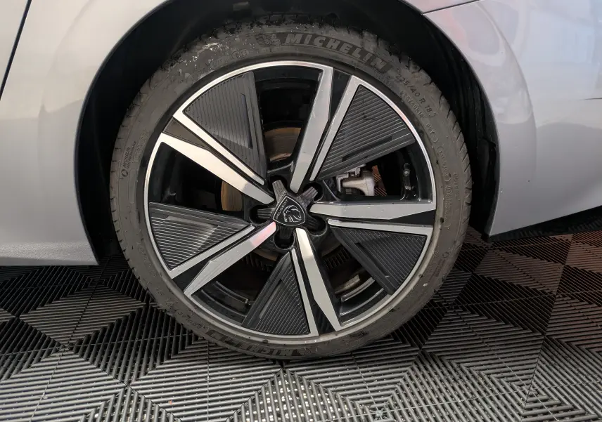 Gros plan sur la roue avant droite gris métallisé d'une Peugeot 308 SW Hybrid 145 eDCS6 GT avec jante alliage 18 pouces bicolore.