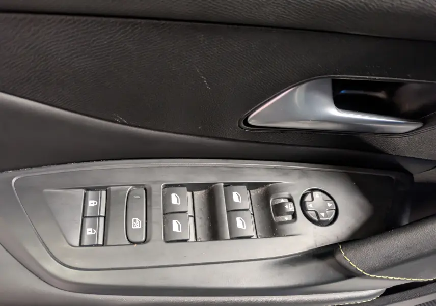Gros plan sur la commande des vitres et rétroviseurs côté conducteur d’un Peugeot 308 SW gris, intérieur noir.