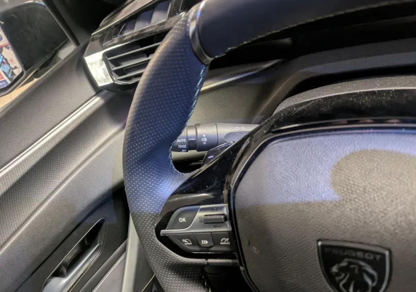 Gros plan sur le volant cuir perforé et les commandes multifonctions du Peugeot 308 SW Hybrid gris, côté conducteur.