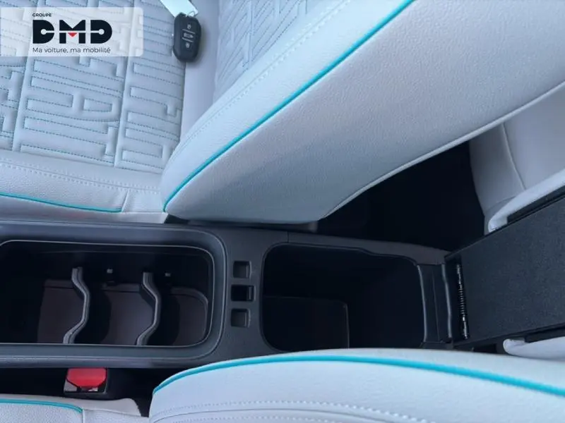 Vue rapprochée de l'accoudoir central ivoire avec surpiqûres bleues et porte-gobelets du Fiat 600 hybride rouge 2026.
