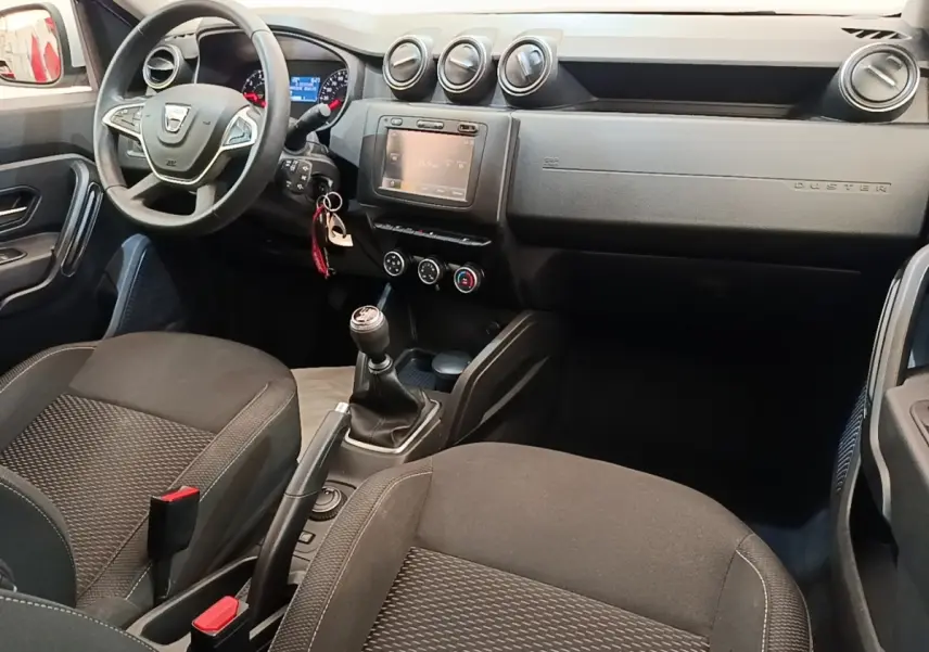 Vue intérieure avant droite du Dacia Duster 2021, tableau de bord noir avec écran tactile et volant multifonctions cuir synthétique.