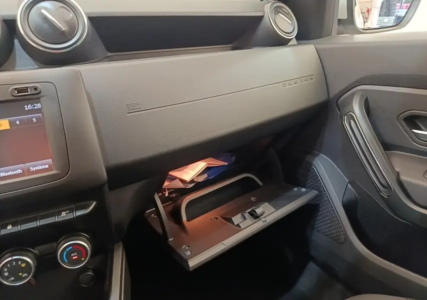Intérieur côté passager du Dacia Duster 2021, vue sur la boîte à gants ouverte et tableau de bord noir.