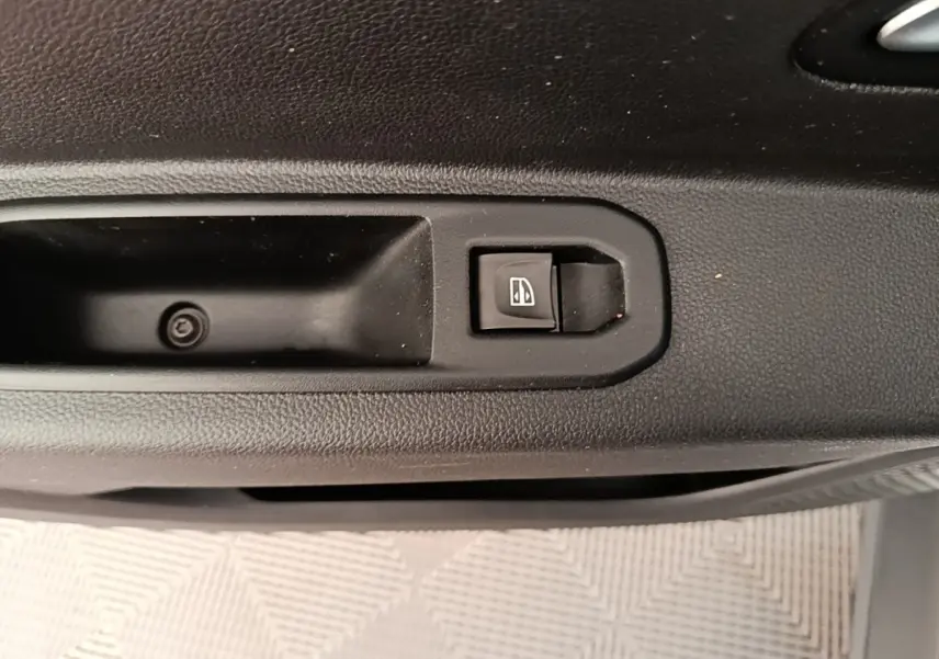 Gros plan sur le bouton de commande de vitre électrique côté conducteur du Dacia Duster blanc, intérieur noir.