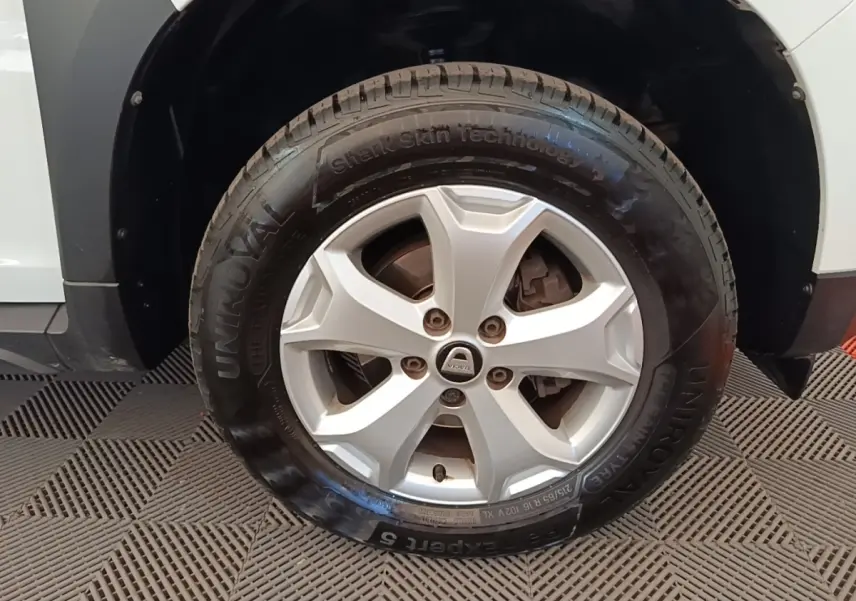 Gros plan sur la roue avant droite d’un Dacia Duster blanc, mettant en valeur la jante argentée et le pneu Uniroyal.