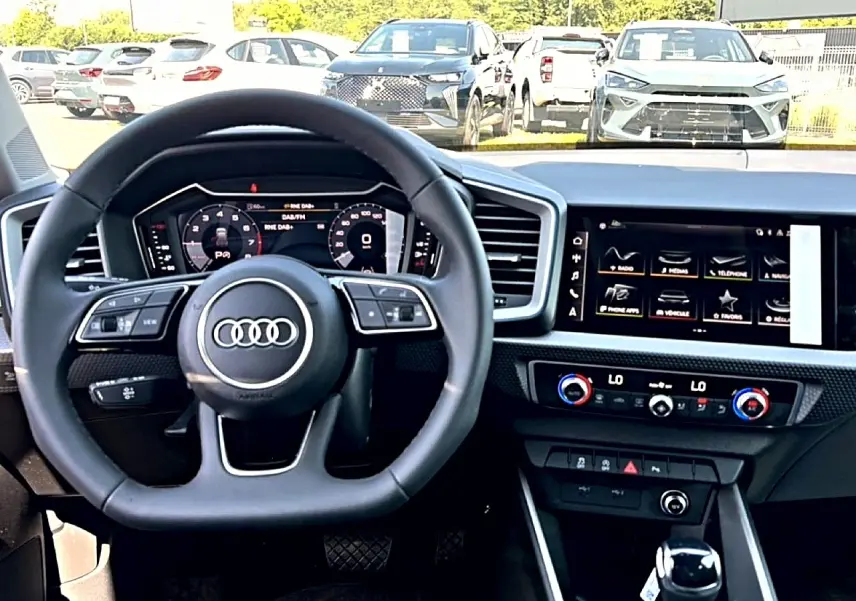 Vue intérieure centrée sur le volant multifonction et l'écran tactile du tableau de bord de l'Audi A1 Sportback blanc/noir.