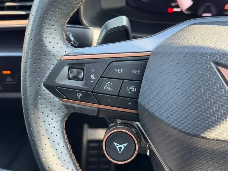 Gros plan sur la partie gauche du volant perforé noir du CUPRA Formentor 1.5 eTSI Hybrid 2025 avec commandes intégrées et logo cuivré.