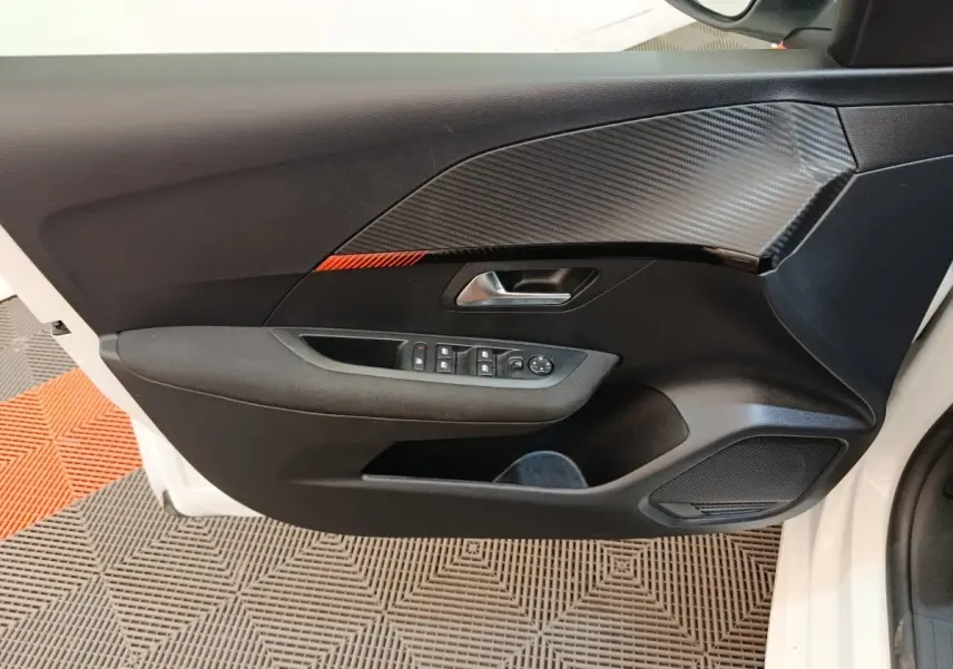 Vue intérieure du panneau de porte avant gauche noir avec insert effet carbone et boutonnerie sur Peugeot 208 blanc 2023.