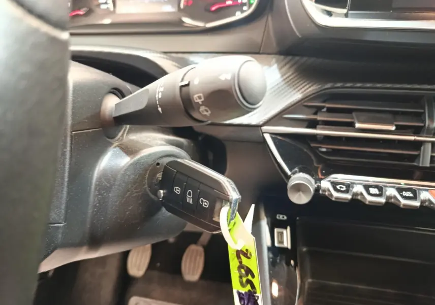 Gros plan intérieur sur le contact et la clé d’une Peugeot 208 blanche, avec tableau de bord et commandes visibles.