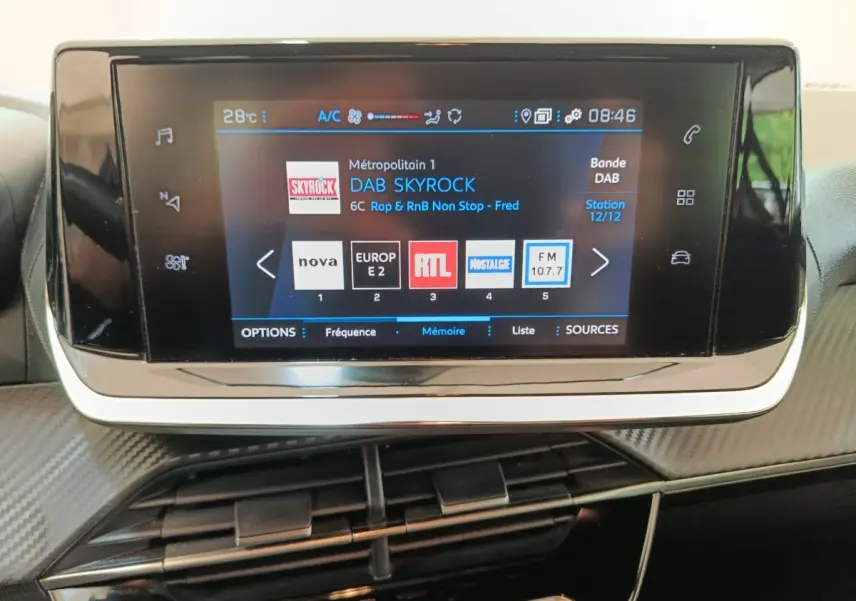 Écran tactile central du tableau de bord de la Peugeot 208 1.5 BlueHDi blanc, affichant les stations radio DAB.
