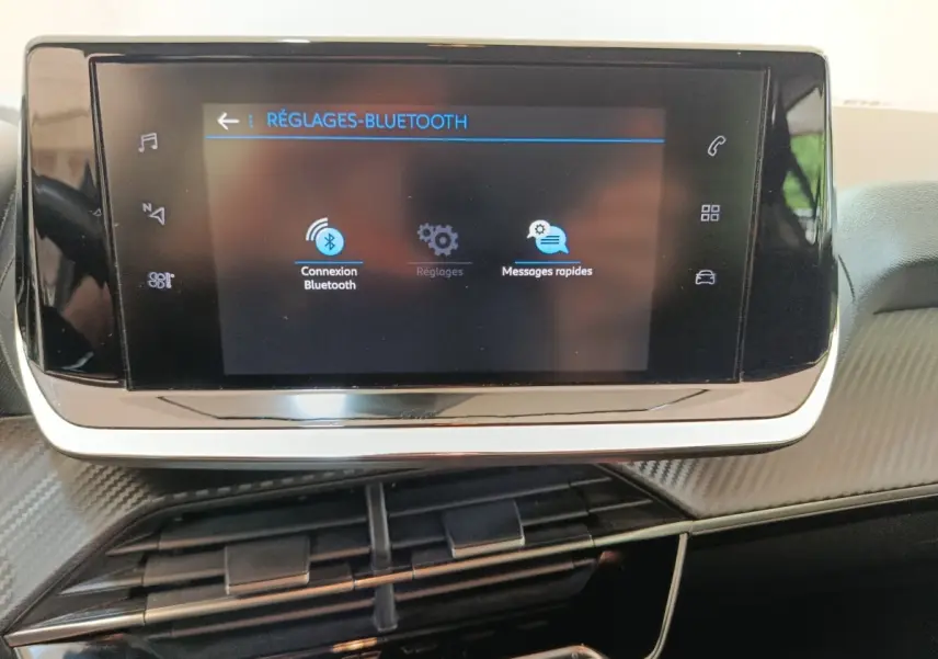 Écran tactile central affichant les réglages Bluetooth dans l’habitacle de la Peugeot 208 blanche, vue de face rapprochée.