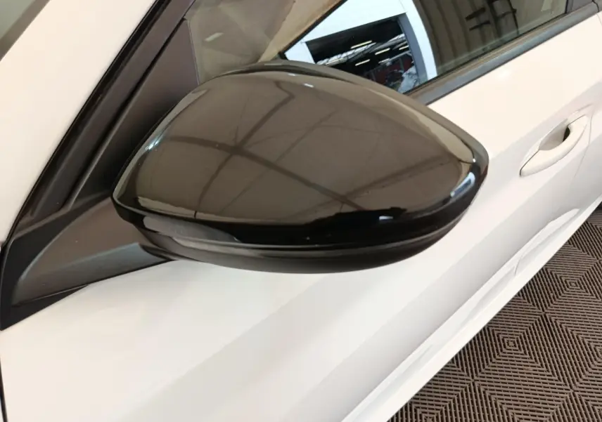 Rétroviseur noir côté gauche en gros plan sur Peugeot 208 blanche vue partielle de la porte avant.