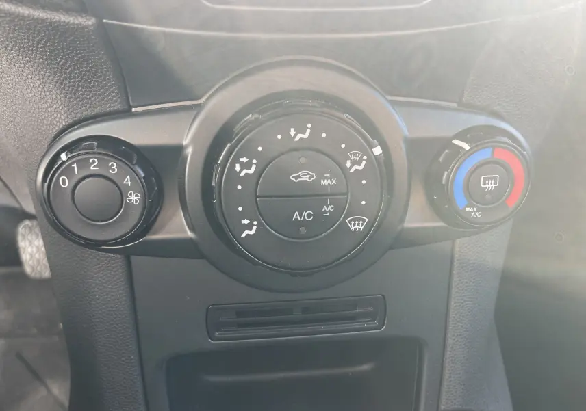 Gros plan sur les commandes de climatisation d'une Ford Fiesta gris titane 2014 avec réglages manuels et bouton de chauffage arrière.