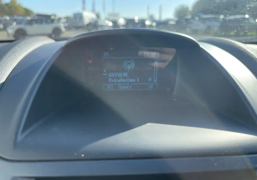 Écran central du tableau de bord de la Ford Fiesta 2014 affichant la radio Oxygène en extérieur lumineux.