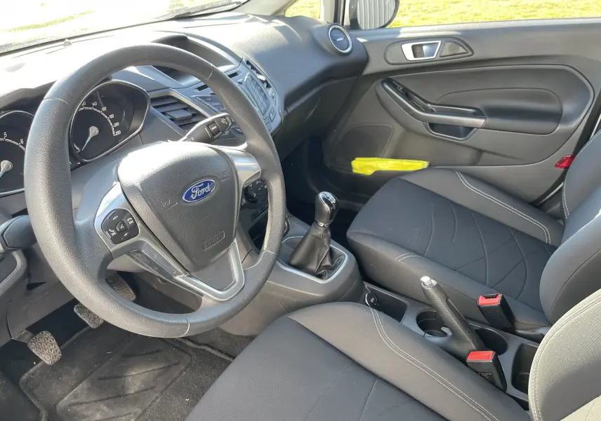 Intérieur avant droit d'une Ford Fiesta gris titane 2014, volant multifonction et boîte manuelle visible.