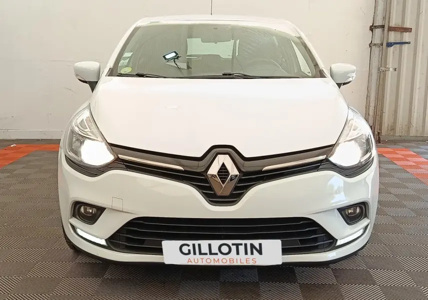 Vue frontale d'une Renault Clio Business dCi 75 blanche avec phares allumés et calandre noire brillante.