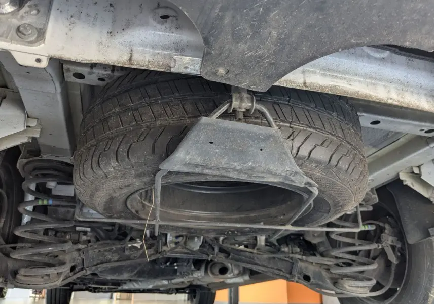 Vue en contre-plongée sous un FIAT Scudo Fourgon blanc, montrant la roue de secours suspendue sous le châssis.