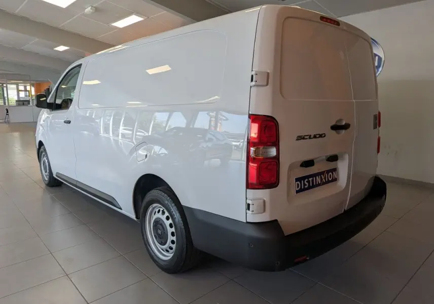 Vue 3/4 arrière droite du fourgon FIAT Scudo blanc avec jantes tôles grises et portes arrière fermées en intérieur showroom.