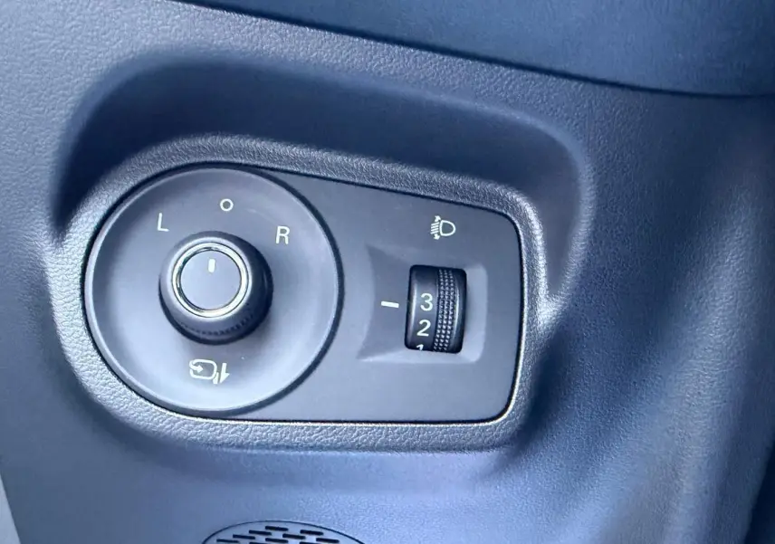 Gros plan sur les commandes de réglage des rétroviseurs et des phares d’un MG3 Pebble Black métallisé, intérieur noir.