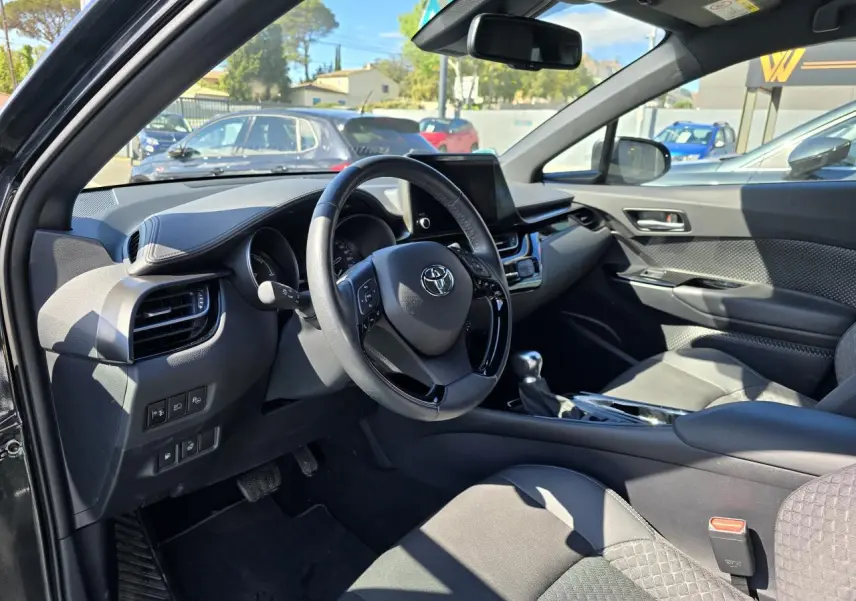 Intérieur côté conducteur du Toyota C-HR noir métal 2023, volant cuir multifonction et écran tactile central visible.