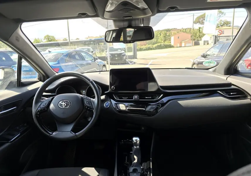 Vue intérieure avant du Toyota C-HR 1.8 Hybride 2023 avec tableau de bord noir et écran tactile central.