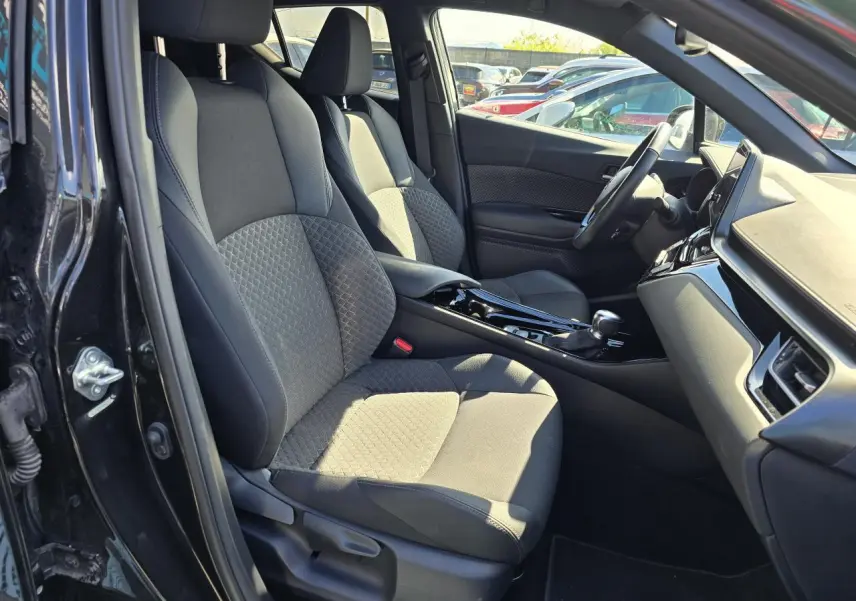 Intérieur côté conducteur du Toyota C-HR noir métal 2023, sièges tissu/cuir avec surpiqûres grises et console centrale brillante.