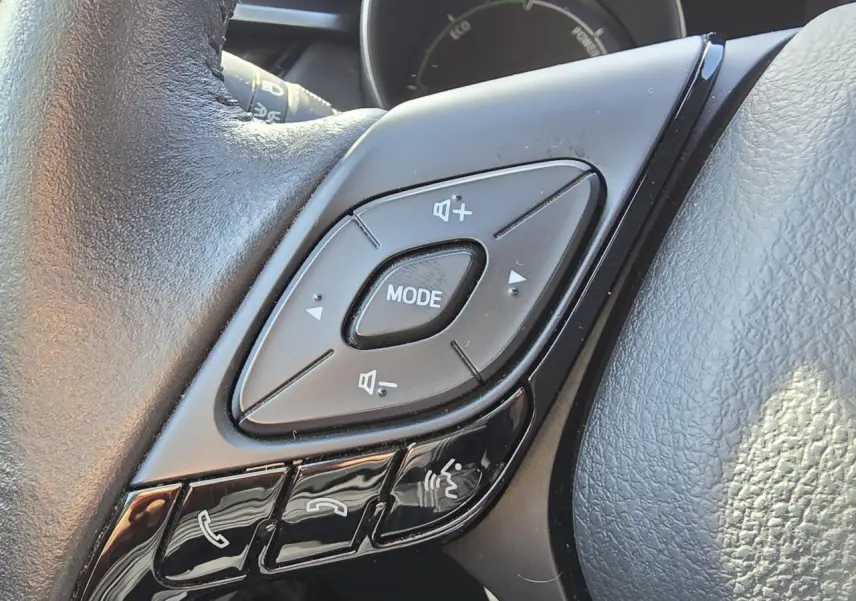 Gros plan sur les commandes multifonctions du volant cuir noir du Toyota C-HR 1.8 Hybride 2023.