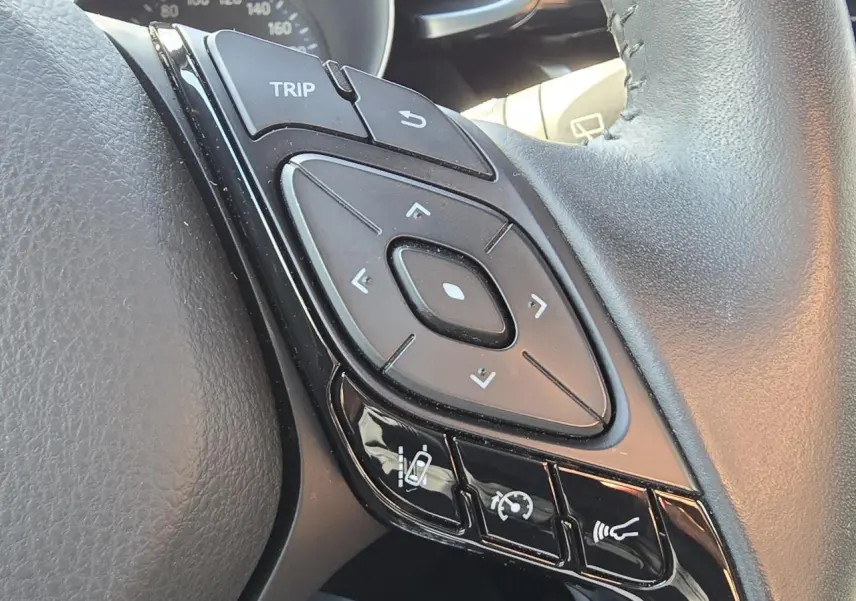 Gros plan sur les commandes multifonctions noires du volant cuir du Toyota C-HR 1.8 Hybride noir métal 2023.