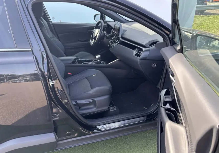 Intérieur côté gauche d'une Toyota C-HR noir métal 2023, sièges tissu/cuir noir avec surpiqûres grises et tableau de bord moderne.