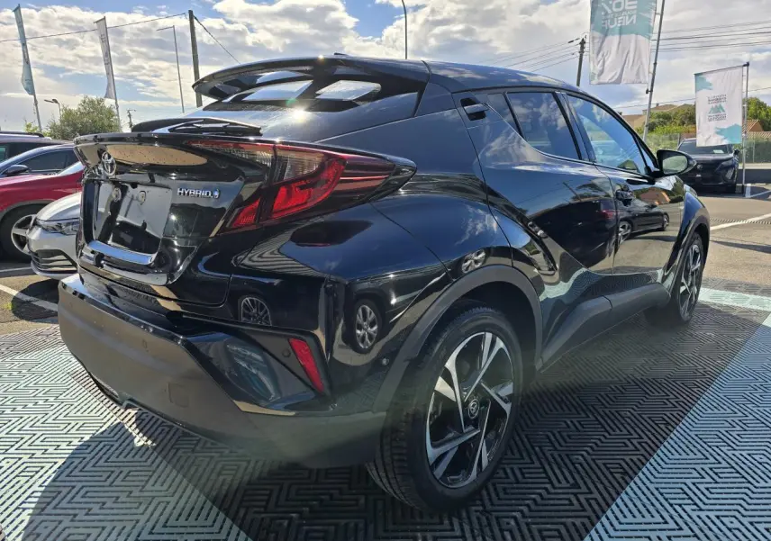 Toyota C-HR noir métal vu en 3/4 arrière droit, avec jantes alliage 18 pouces et becquet avant couleur carrosserie.