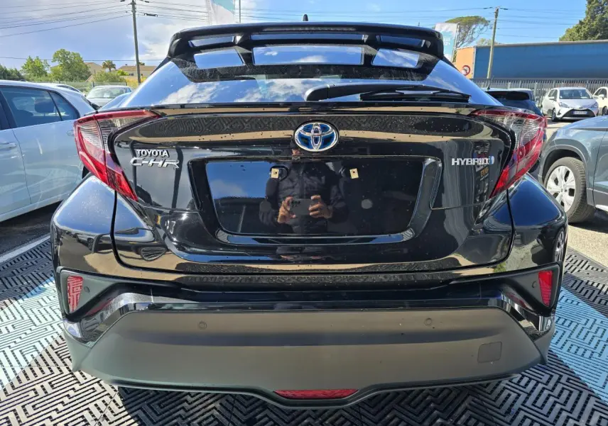 Vue arrière d'un Toyota C-HR noir métal hybride 2023 avec becquet et feux arrière distinctifs en forme angulaire.