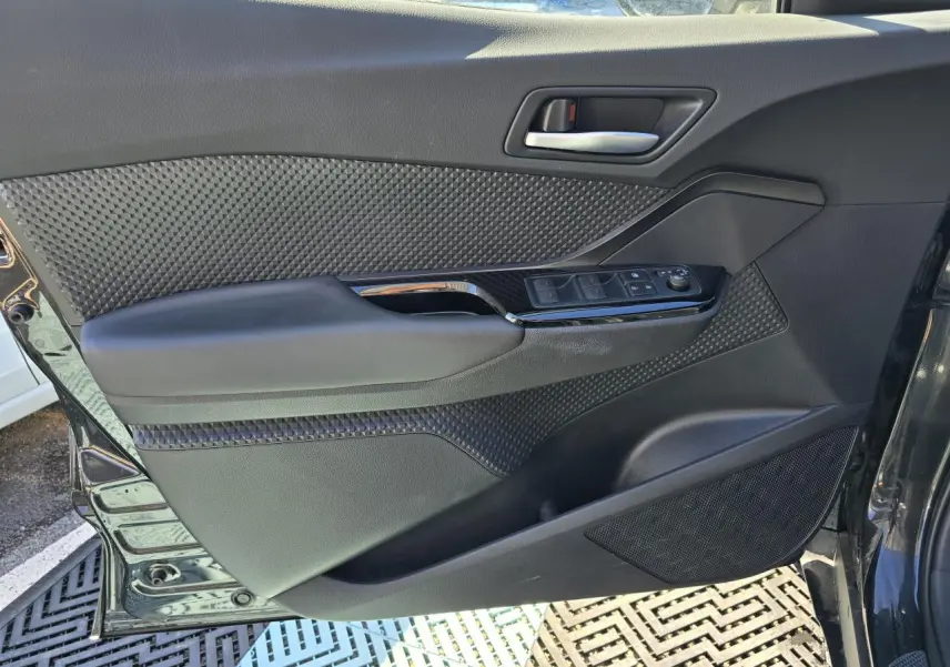 Porte avant gauche ouverte du Toyota C-HR noir métal 2023, avec commandes électriques et garniture texturée.