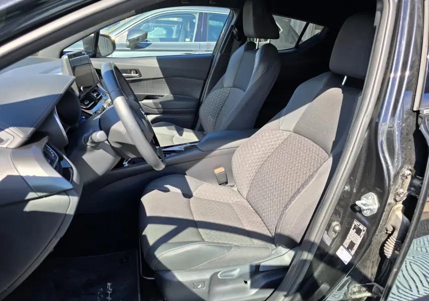 Vue intérieure côté conducteur du Toyota C-HR 2023 noir métal, sièges tissu/cuir avec surpiqûres grises et console centrale moderne.