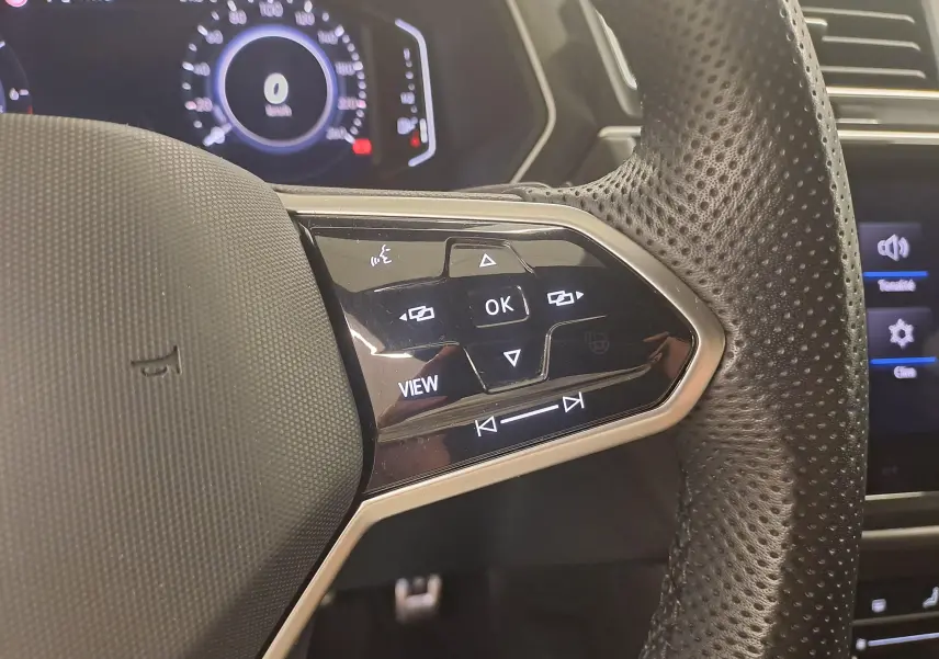 Gros plan sur la partie droite du volant perforé du Volkswagen Tiguan 1.4 eHybrid blanc avec commandes multifonctions et tableau de bord numérique.