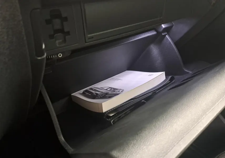 Gros plan sur la boîte à gants ouverte du Volkswagen Tiguan 1.4 eHybrid blanc, avec manuel et pochette à l'intérieur.