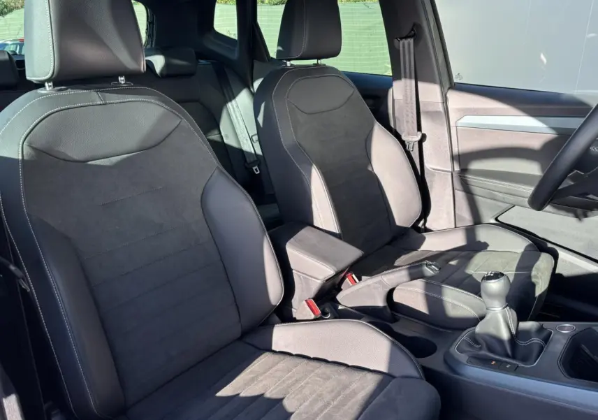 Vue intérieure côté conducteur et passager avant du SEAT Arona 2025, sièges en cuir noir avec surpiqûres blanches et levier de vitesses manuel.